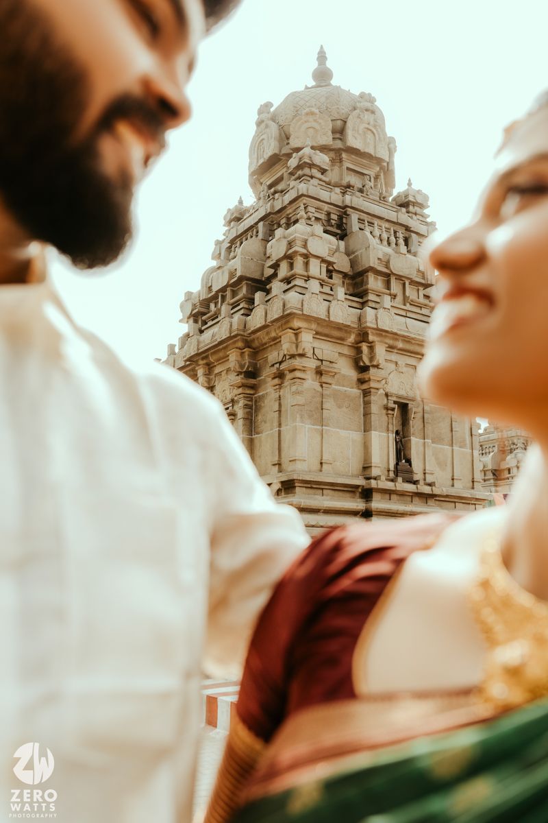 Indian couple in traditional attire share a romantic moment with ancient temple gopuram in background.