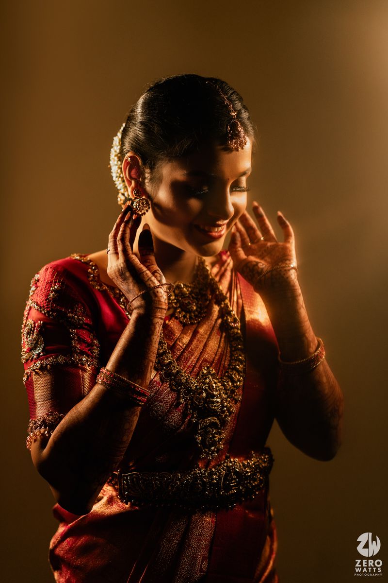 South Indian bride in red silk saree with gold jewelry smiling gracefully during bridal portrait session.