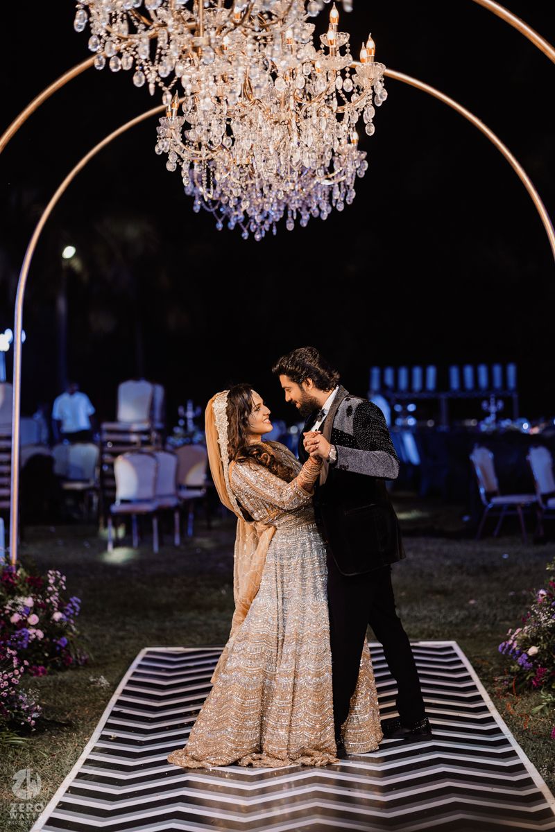 Couple dancing under luxurious crystal chandeliers on a black and white striped dance floor at night.