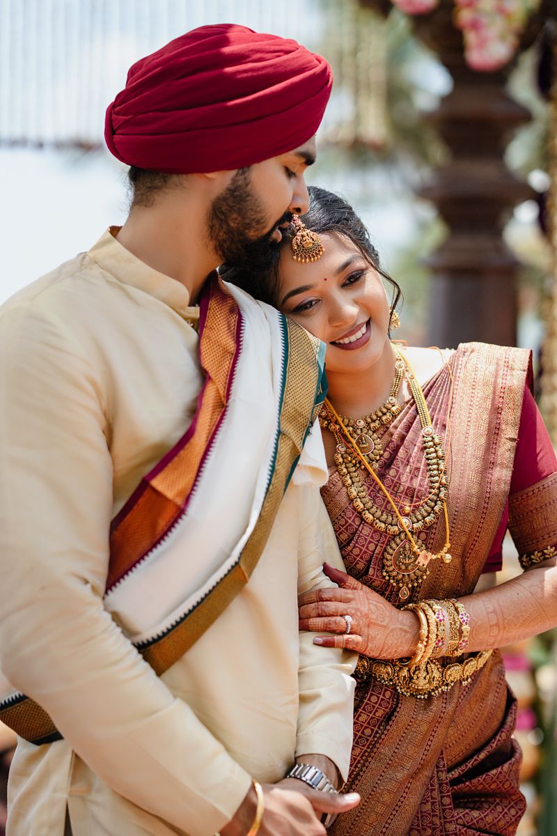 Wedding couple in traditional Indian attire sharing an intimate moment under decorative hanging elements.