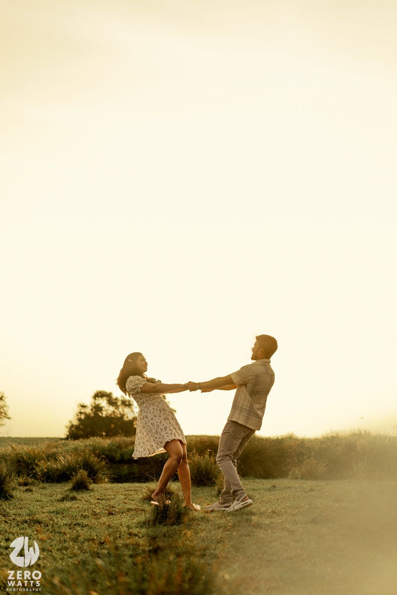 A couple sits in a field at sunset enjoying a romantic moment together in a dreamy, backlit scene.
