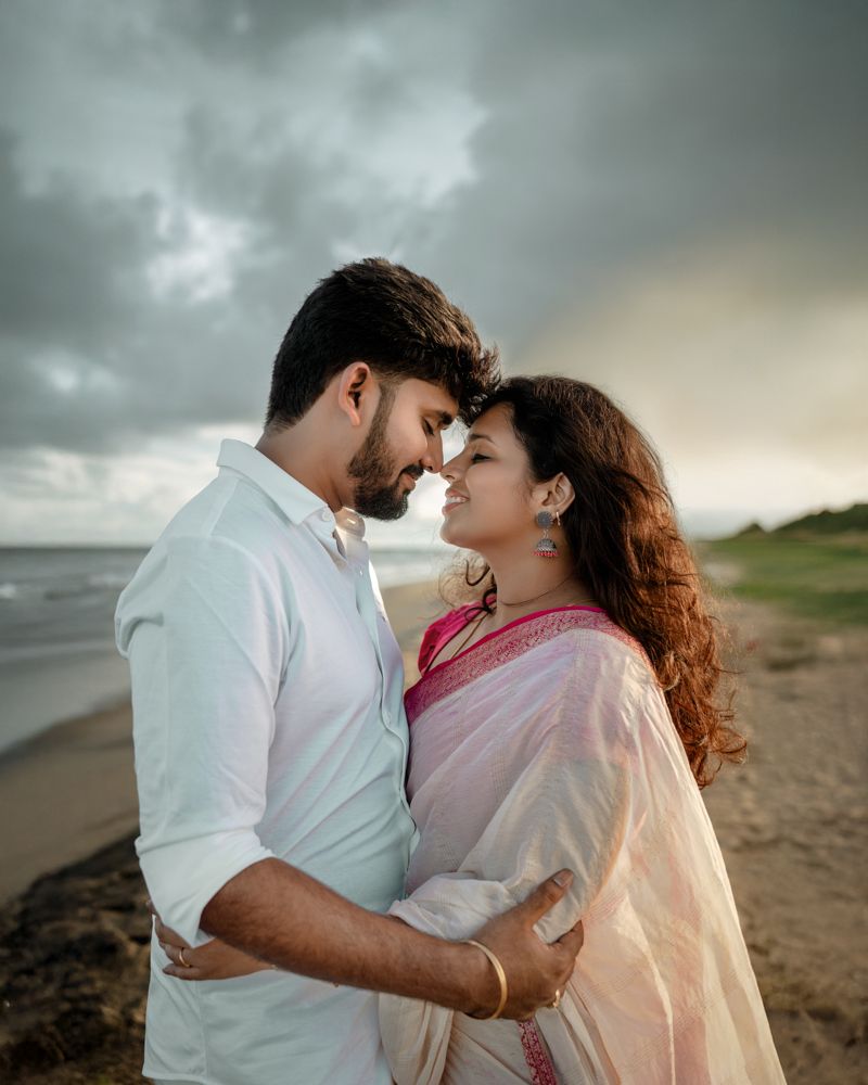 Tender embrace photographed on sandy beach with dramatic stormy sky backdrop.