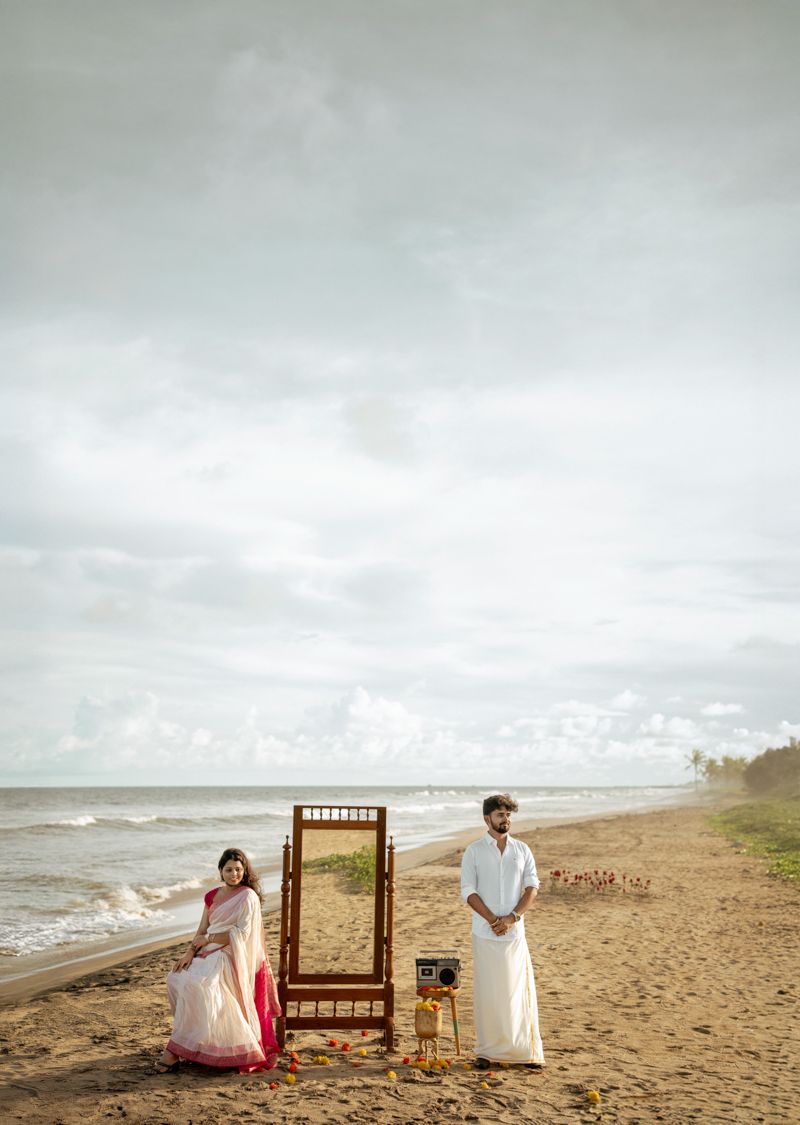 Artistic beach photoshoot setup with wooden mirror and props against a cloudy oceanside backdrop.
