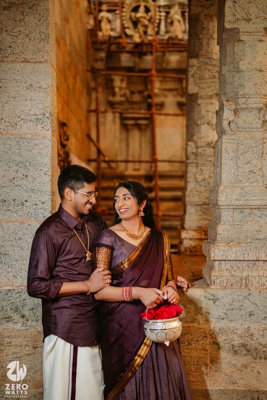 Romantic couple in coordinated burgundy outfits posing against ancient temple pillars and architecture.