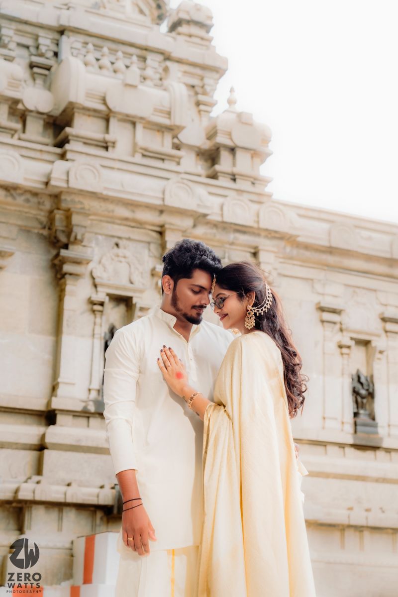 Couple in traditional cream outfits share intimate moments against ornate temple architecture.