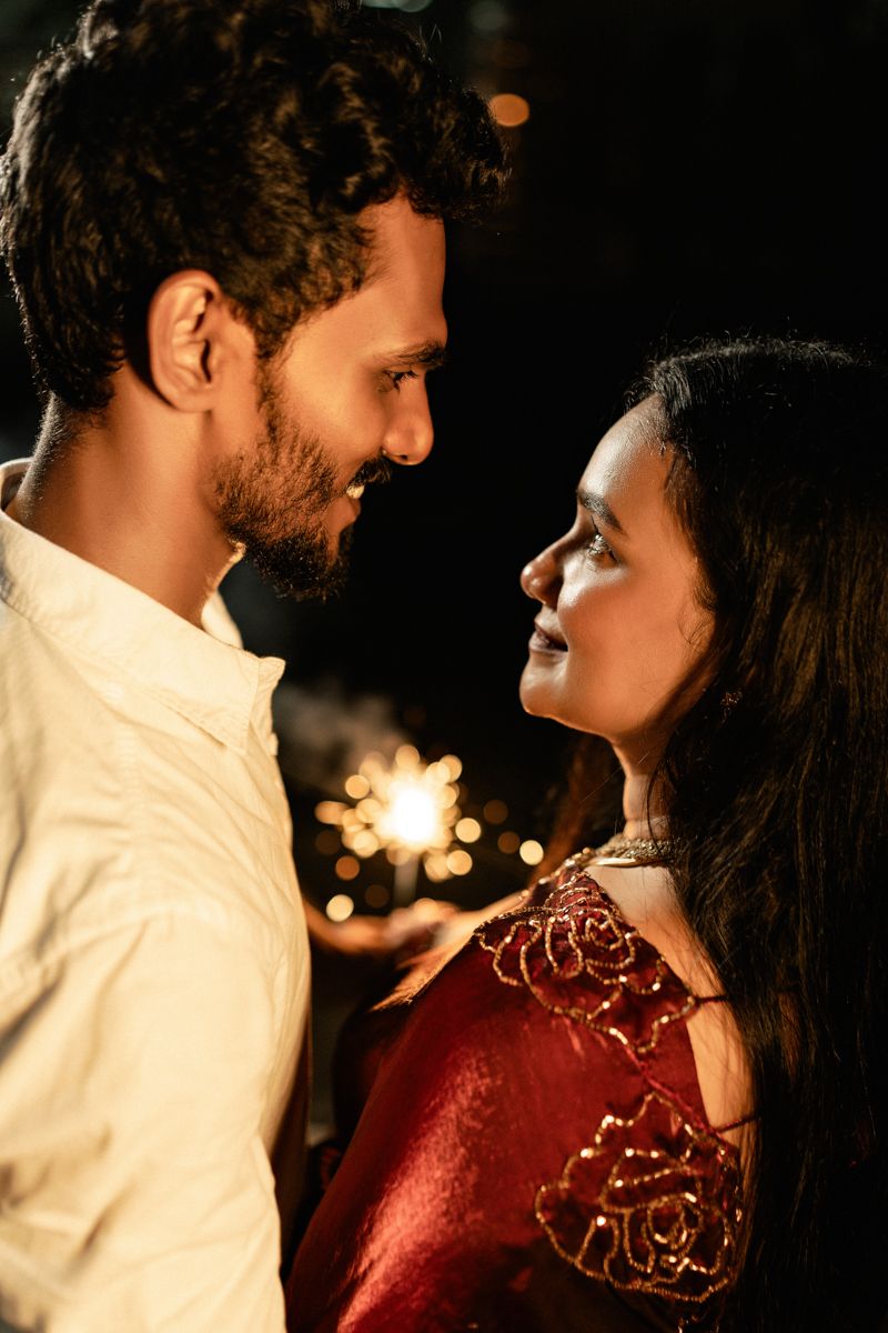 Romantic nighttime portrait with sparklers creating a warm glow against dark background.