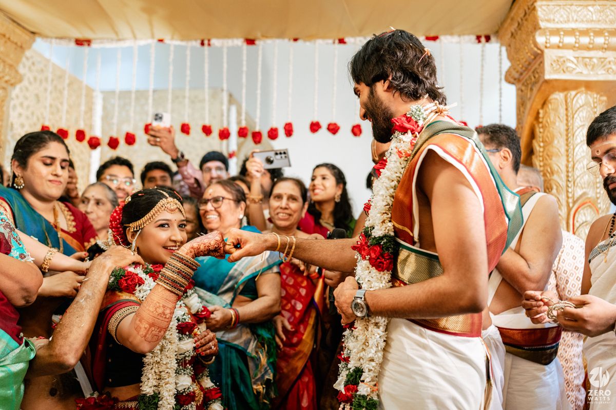 Traditional South Indian wedding ceremony with bride and groom exchanging garlands surrounded by joyful family members.