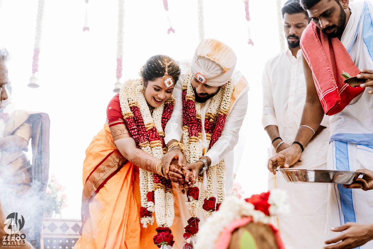 South Indian couple performing sacred fire ritual during traditional wedding ceremony with priest and guests.