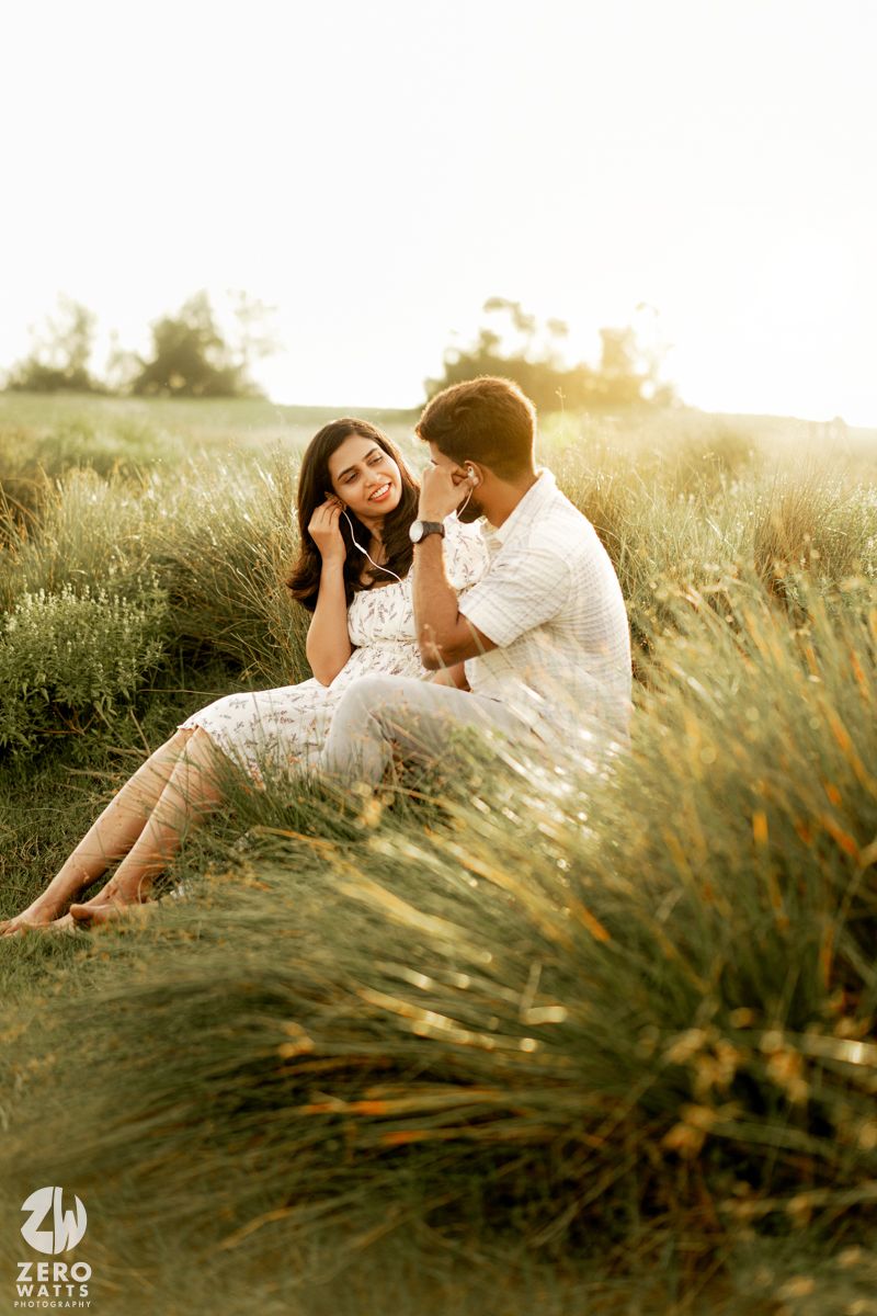 A romantic couple sits together in a sun-drenched meadow of tall grass during golden hour.