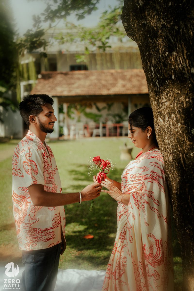 A couple shares an intimate moment under a large tree in matching red and white outfits.