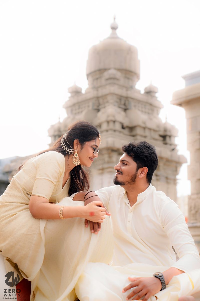 A romantic couple in traditional Indian attire share tender moments against a backdrop of ornate white domed architecture.