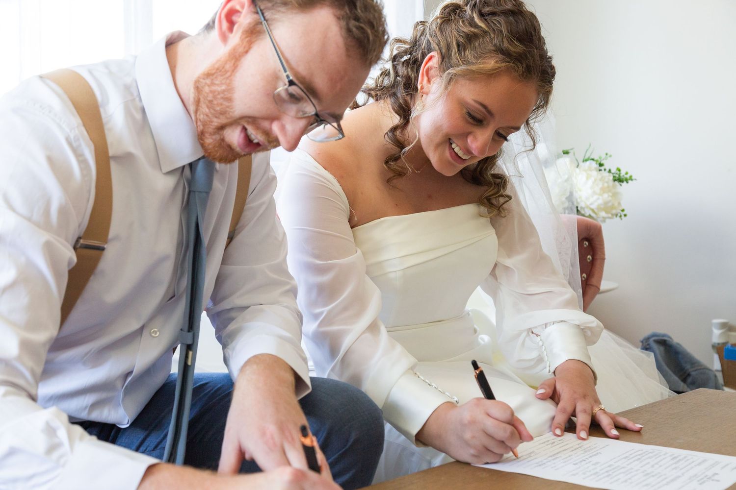 A bride and groom share a happy moment while signing their marriage certificate at their wedding ceremony.