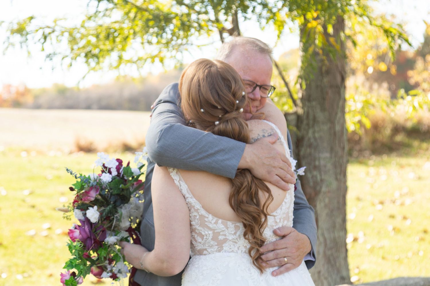 An emotional outdoor autumn embrace under a tree, with a colorful purple and pink bouquet in the foreground.