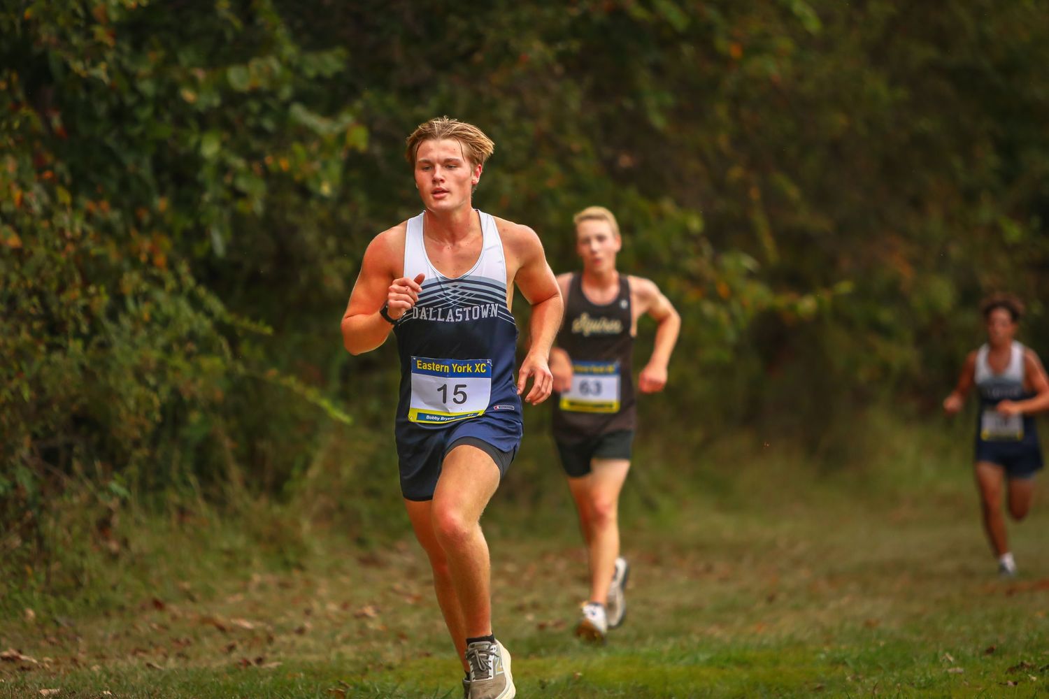 Cross country athletes running along a wooded trail during a competition.