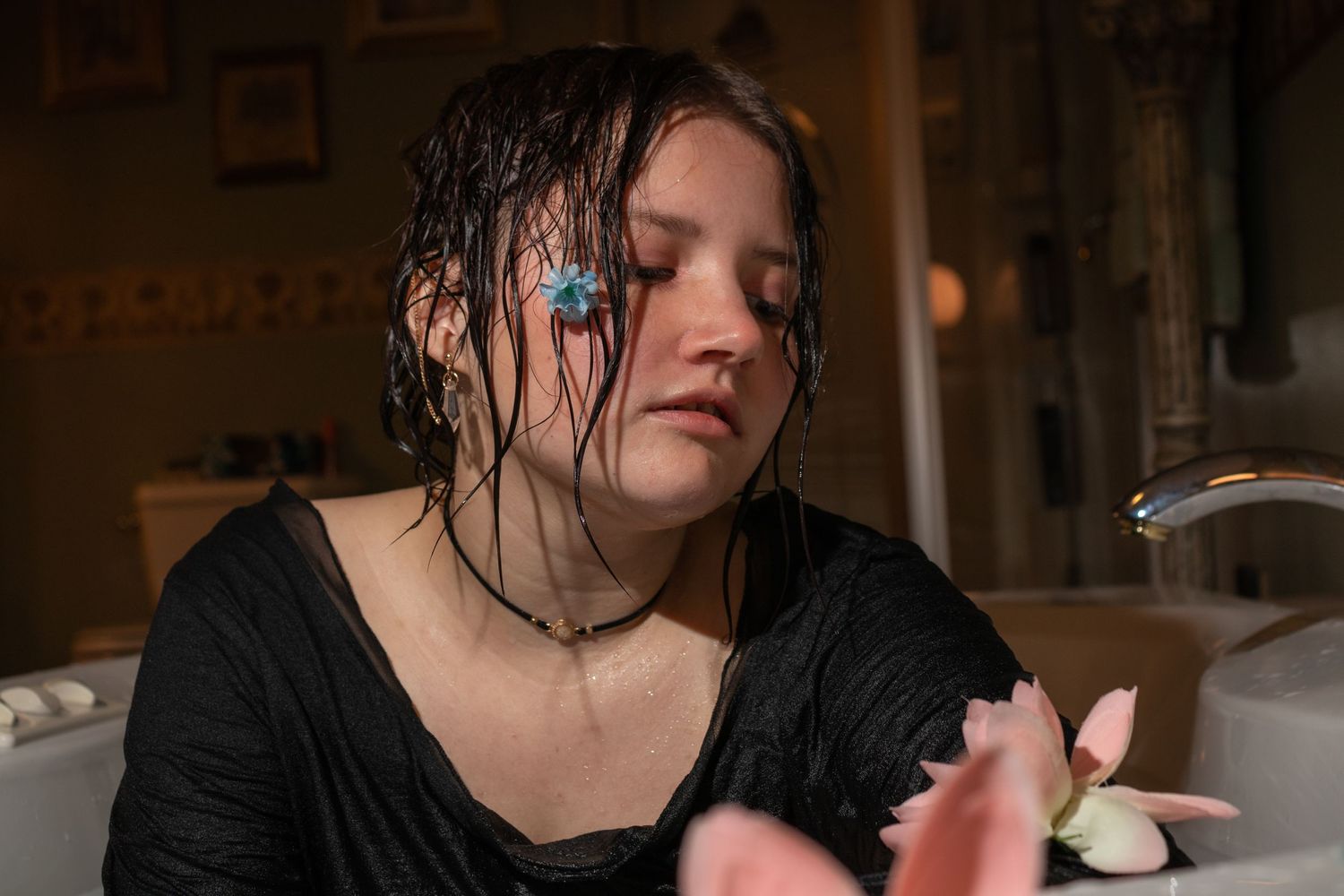 A dramatic milk bath portrait with wet hair and dark clothing in moody lighting.