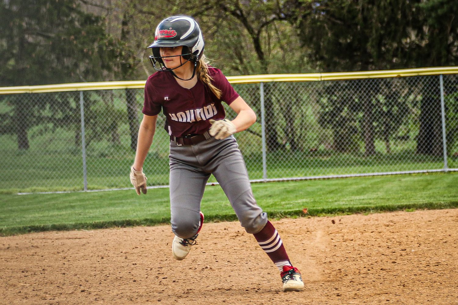 Softball player in Hounds uniform running between bases during game.