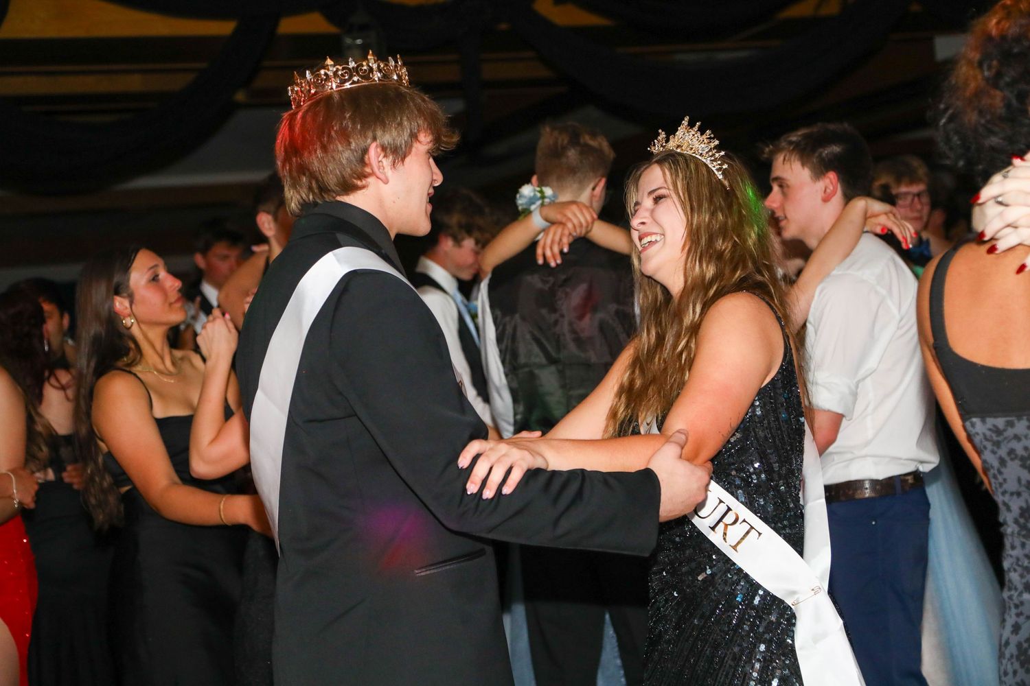Couples dancing at a formal celebration with decorative crowns and formal attire.