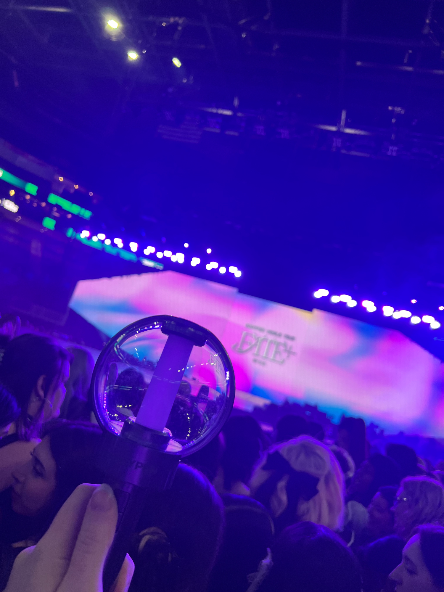 Enhypen lightstick reflects colorful purple and blue lighting in a dark nightclub setting.