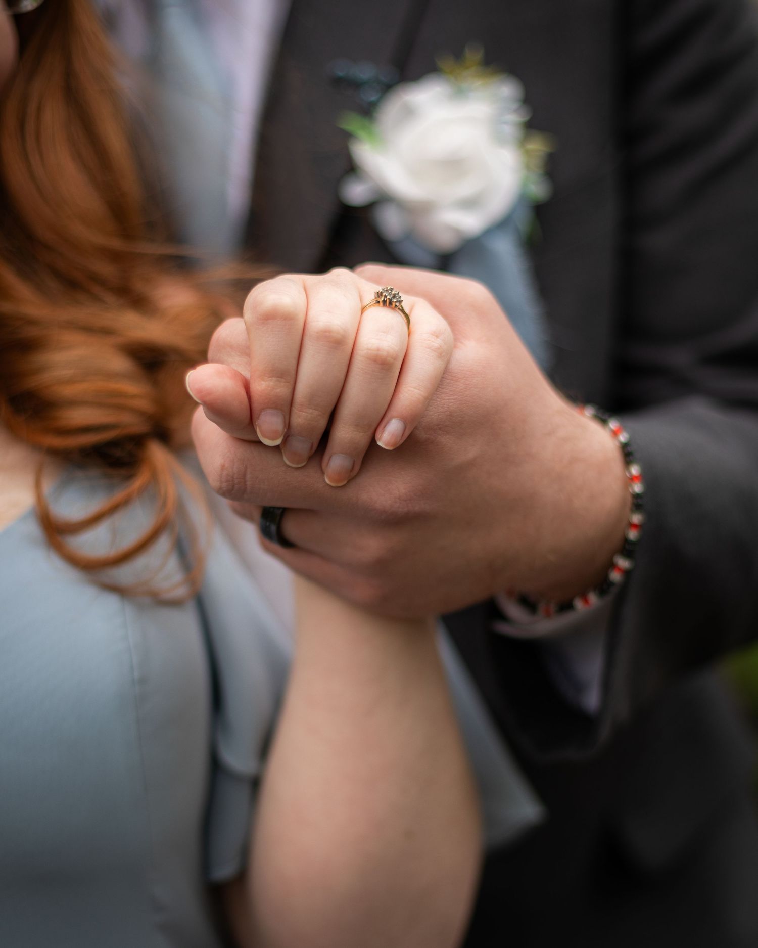 Detail shot of hands holding with engagement ring and boutonniere visible.