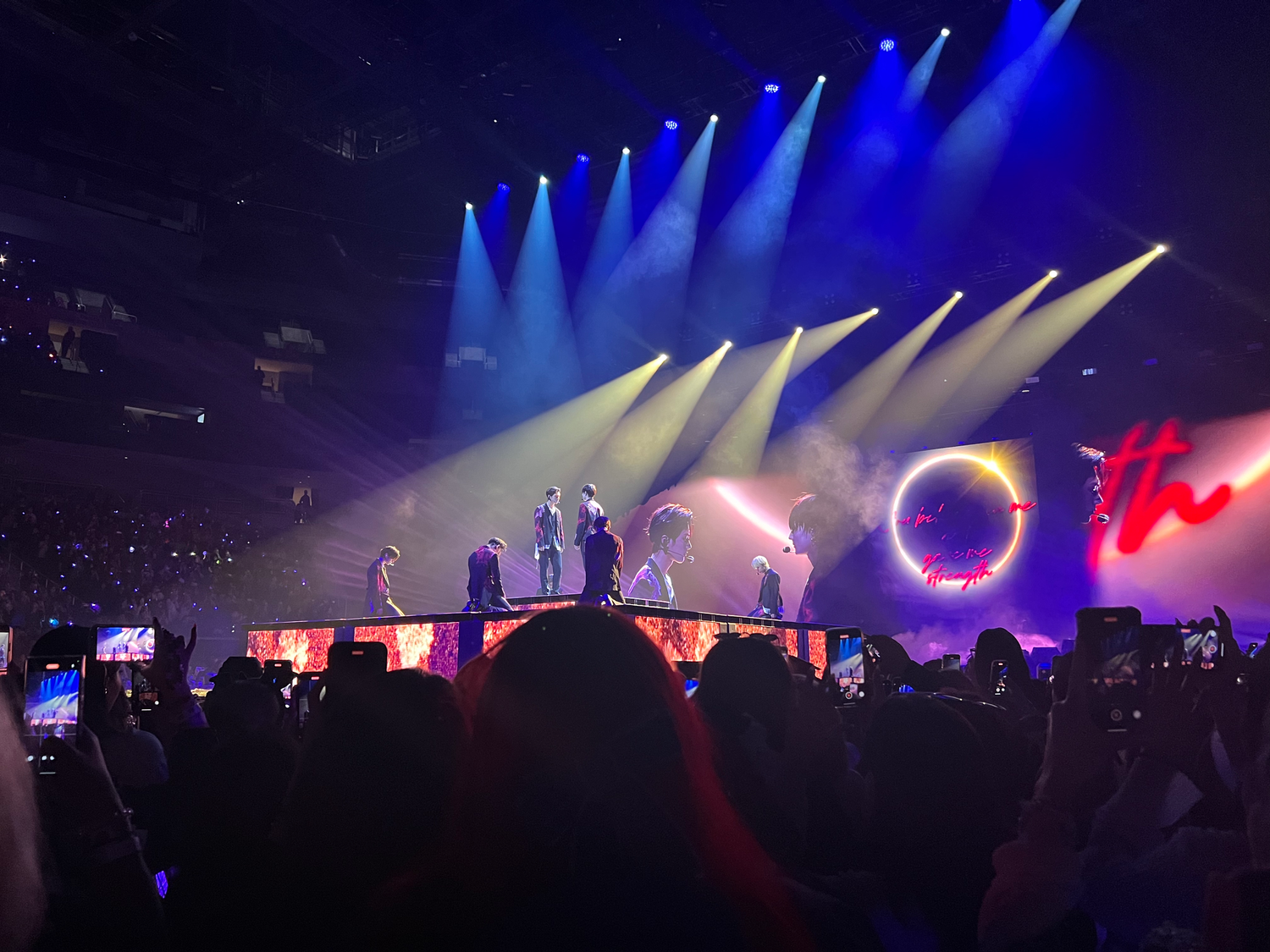 Silhouetted performers on stage with dramatic blue spotlights and circular projection screen.