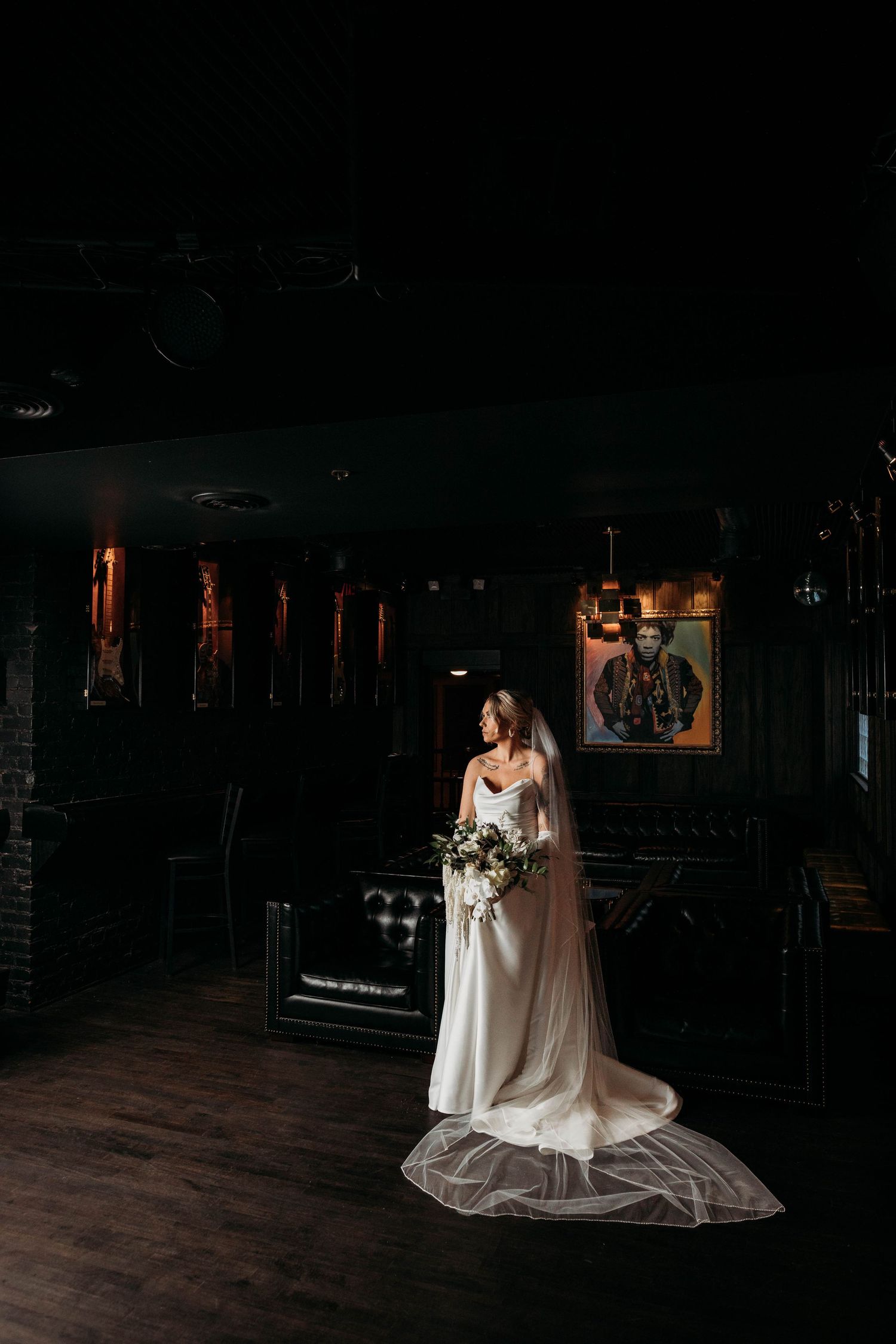 A wedding dress silhouette glows against dark wooden floors in a dim indoor venue.