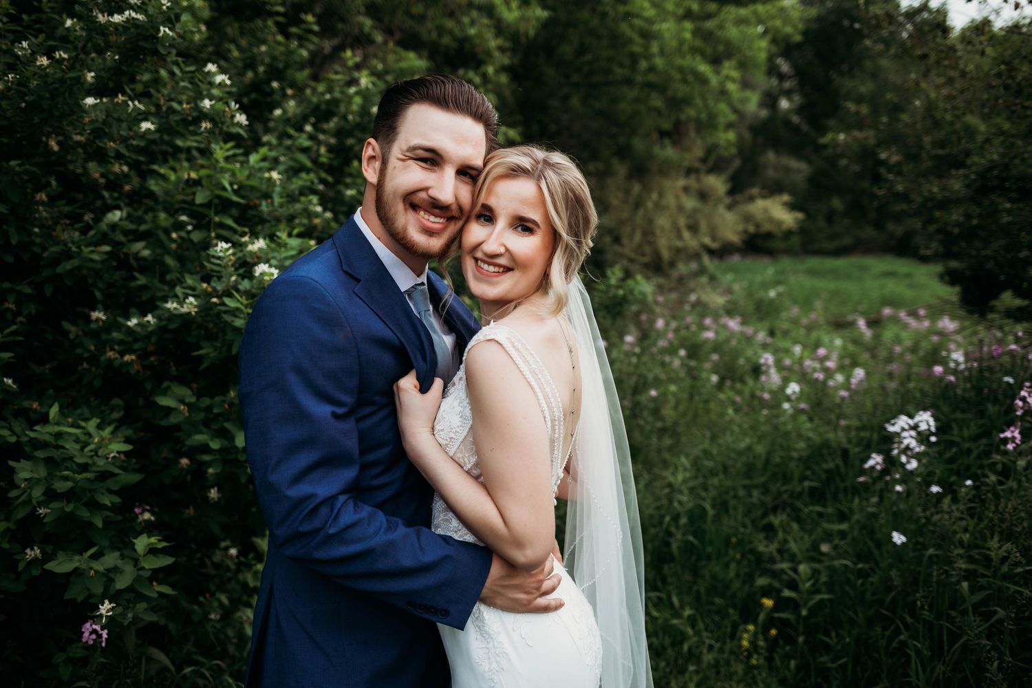 Joyful wedding couple laughing and embracing in garden setting with natural greenery backdrop.
