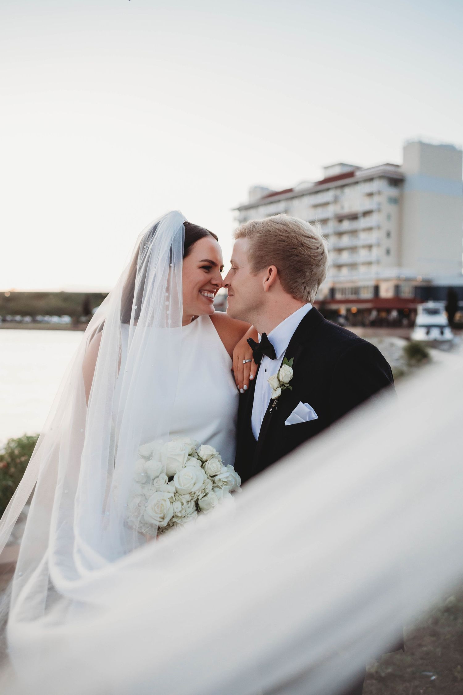 Artistic wedding photo with flowing veil in foreground as couple shares intimate moment.
