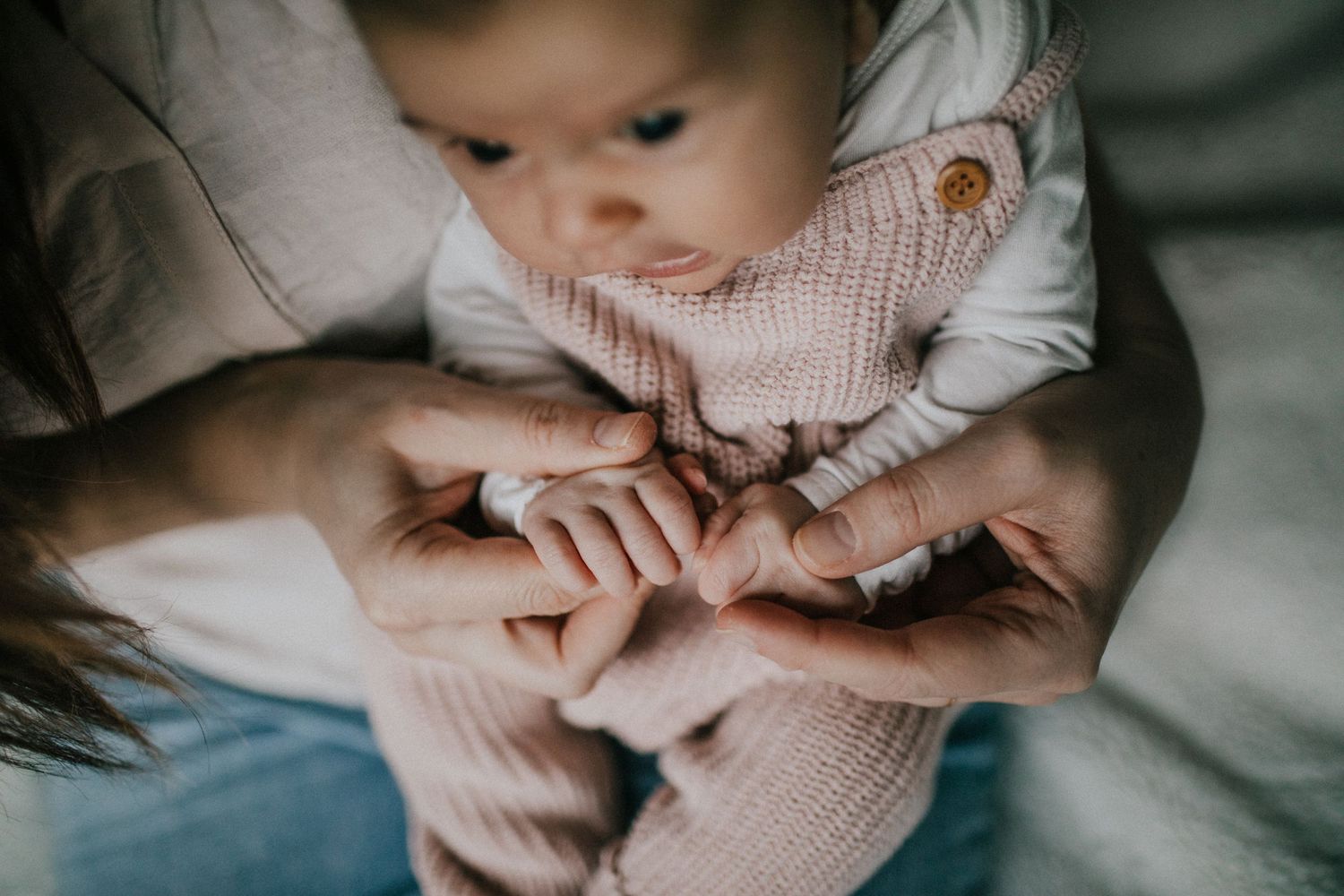 Image of a baby girl looking down at mom holding her hands.