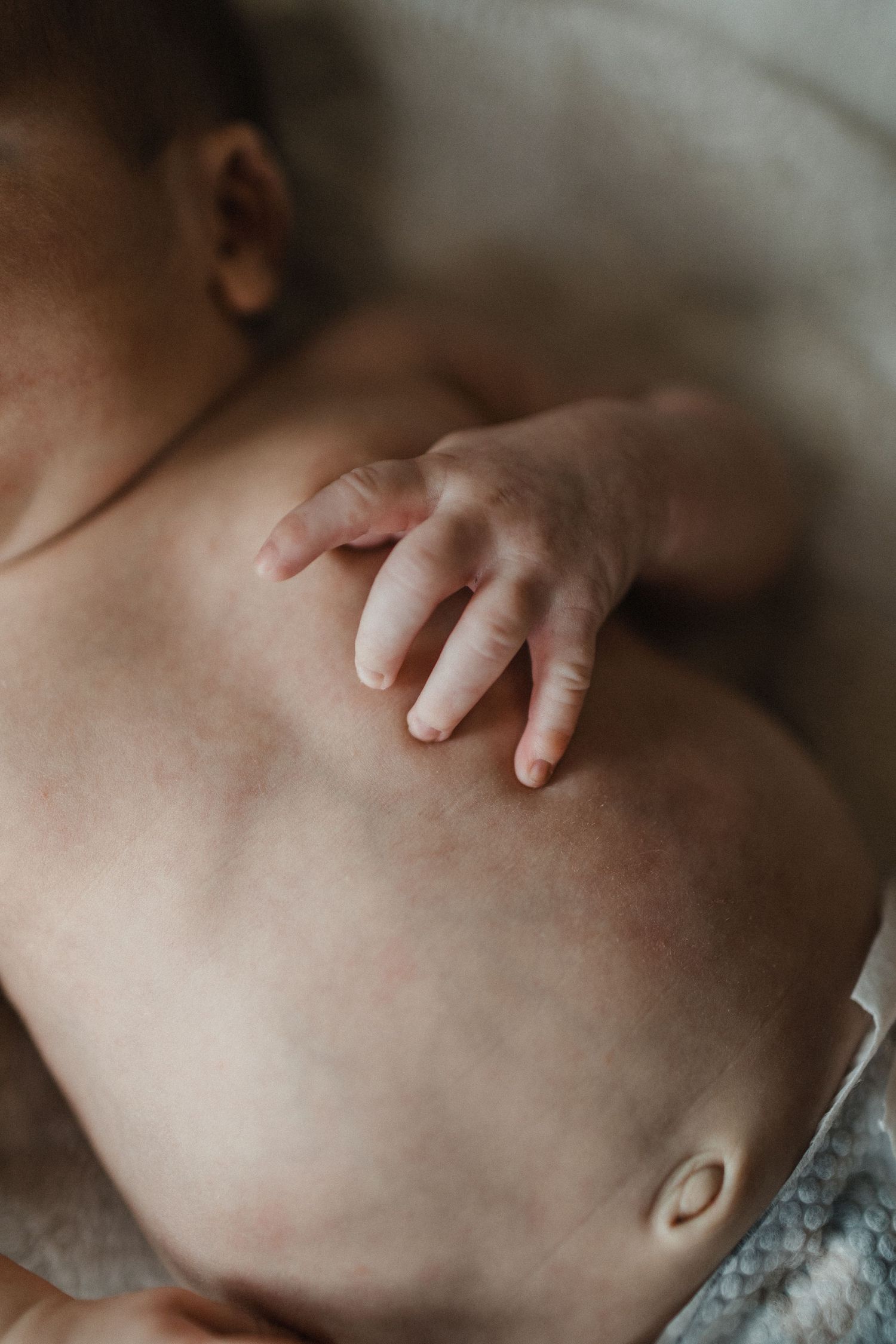 Image of newborn baby's torso with a focus on the stomach and hand.