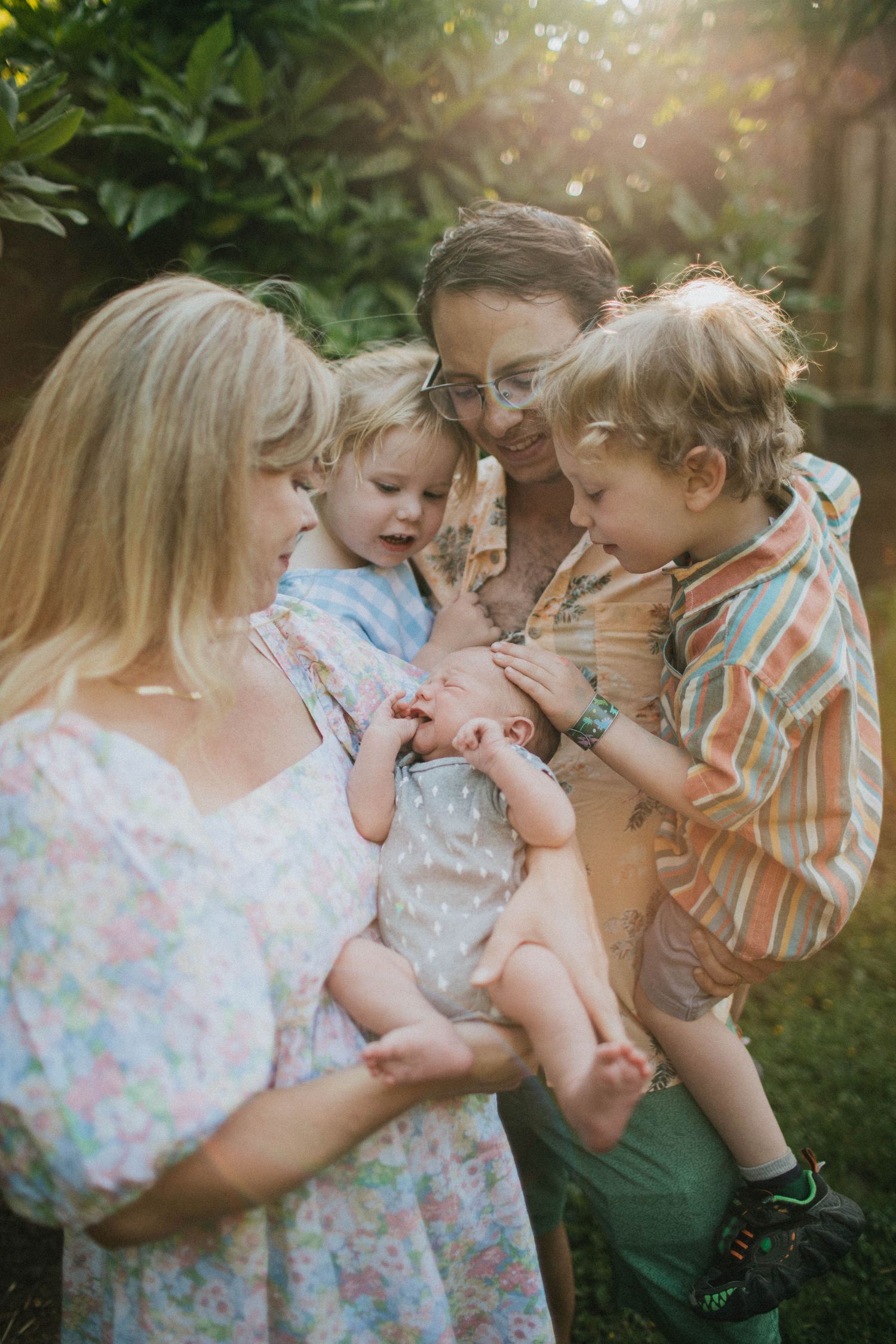 Image of a mom, dad, brother and sister, all looking at the new addition to their family: a baby boy.