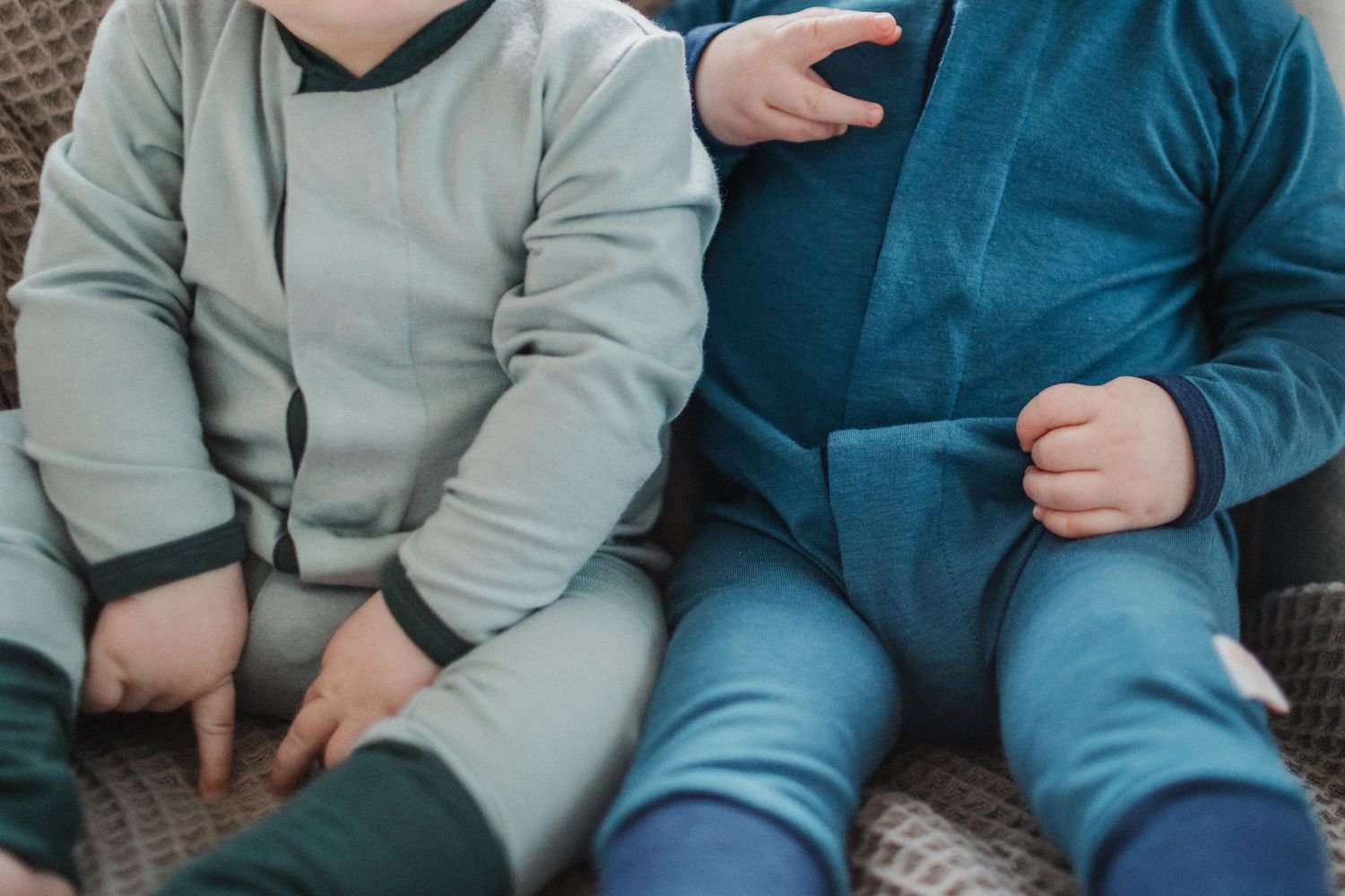 Two babies wearing blue and aqua rompers. Only the outfits are seen; no head or feet.