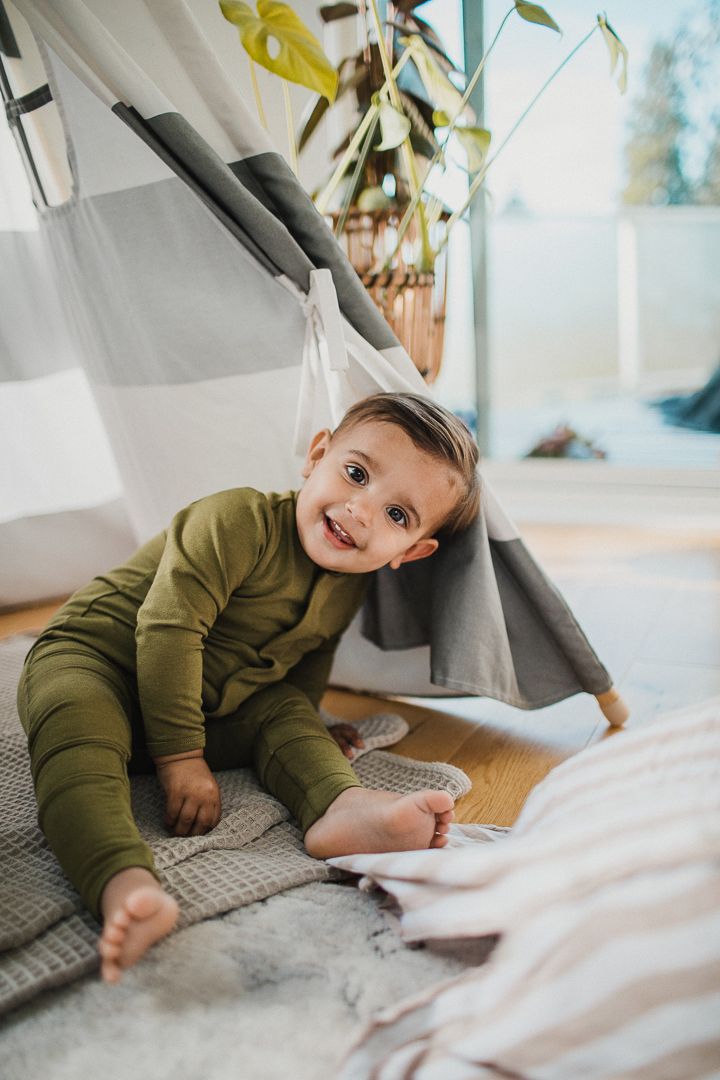 Image of a toddler boy playfully sitting and smiling at the camera wearing a green onesie.