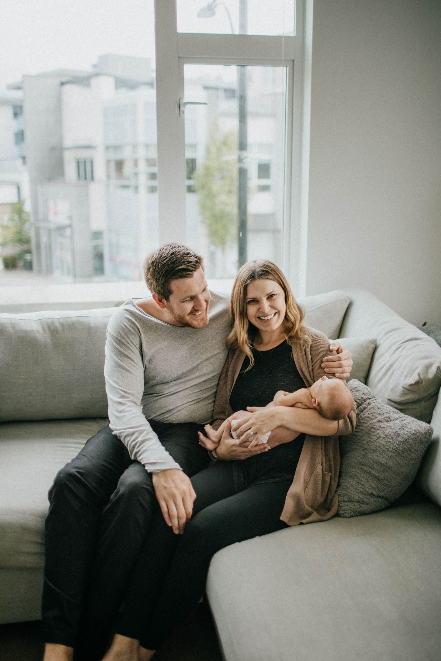 Image of a mom and dad and their newborn baby sitting on a couch.