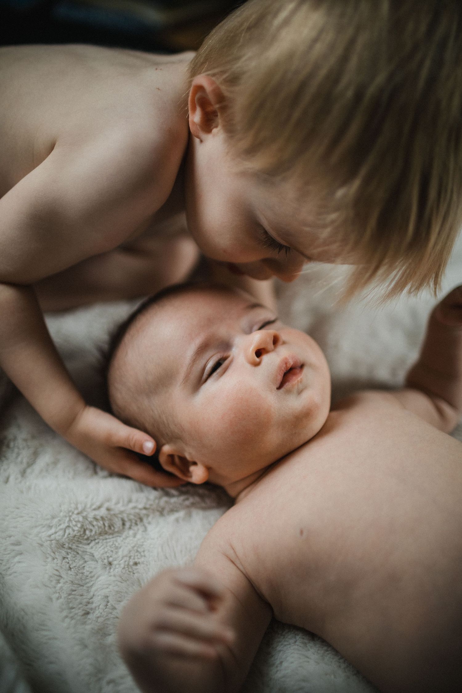 Image of new big brother kissing newborn baby brother on forehead.