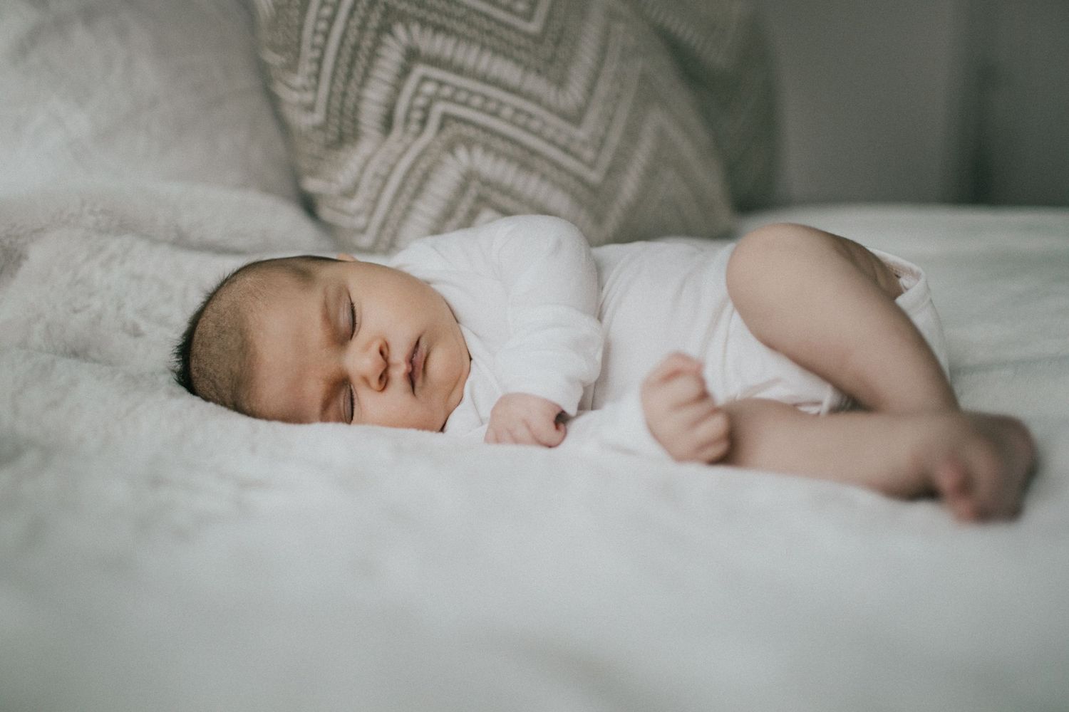 Image of a baby asleep on her side on white fluffy blankets.