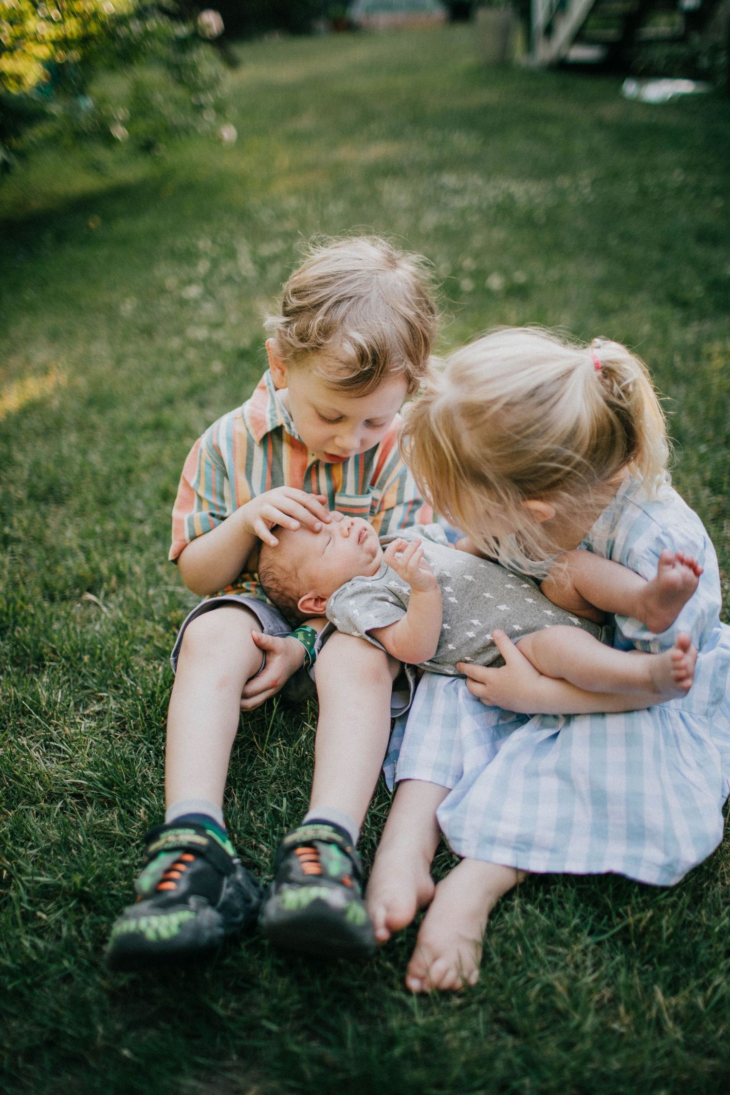 Image of two older siblings, a boy and a girl, holding their new baby brother.