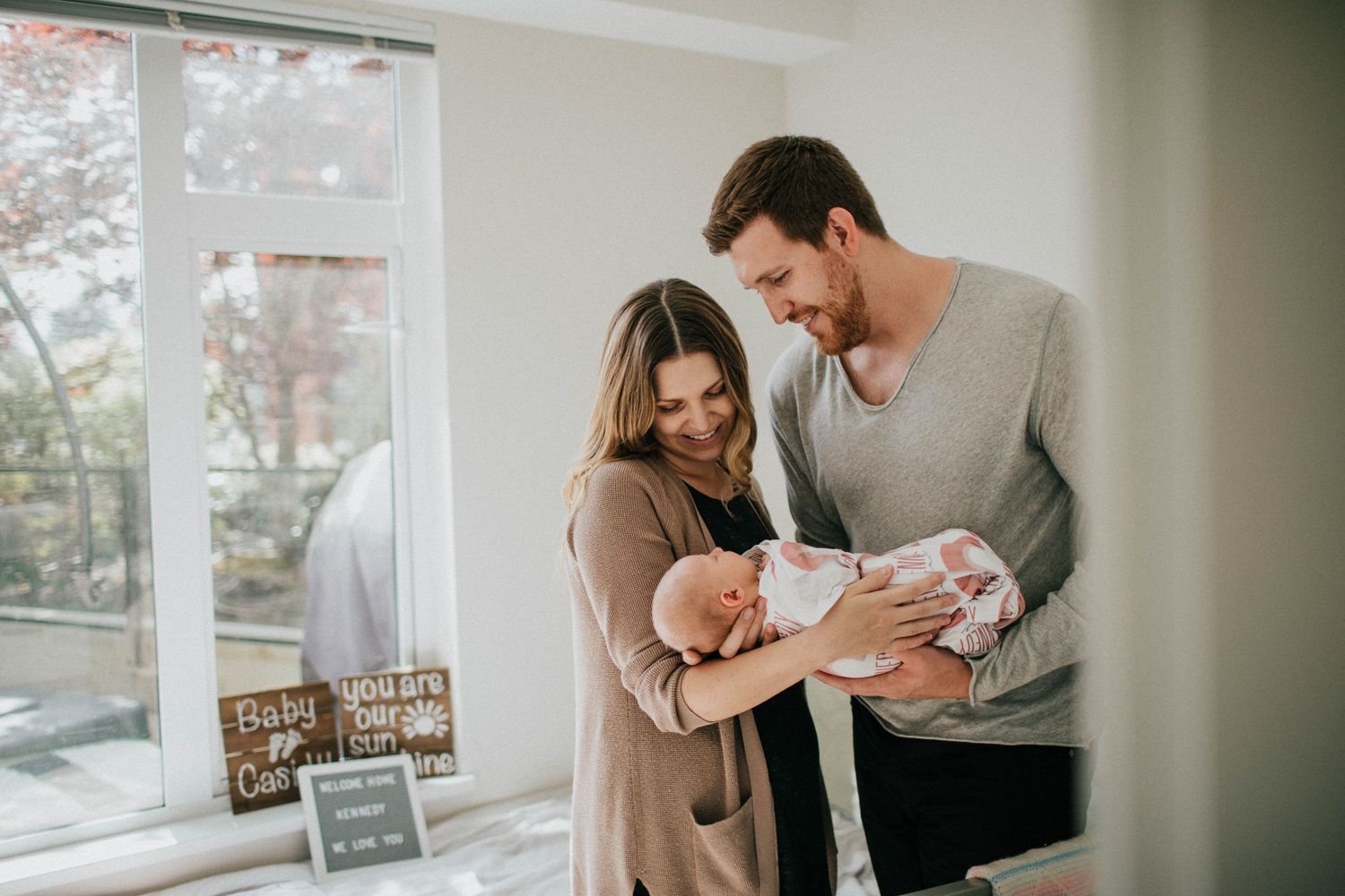 Image of mom and dad standing in nursery while looking at their newborn baby girl.