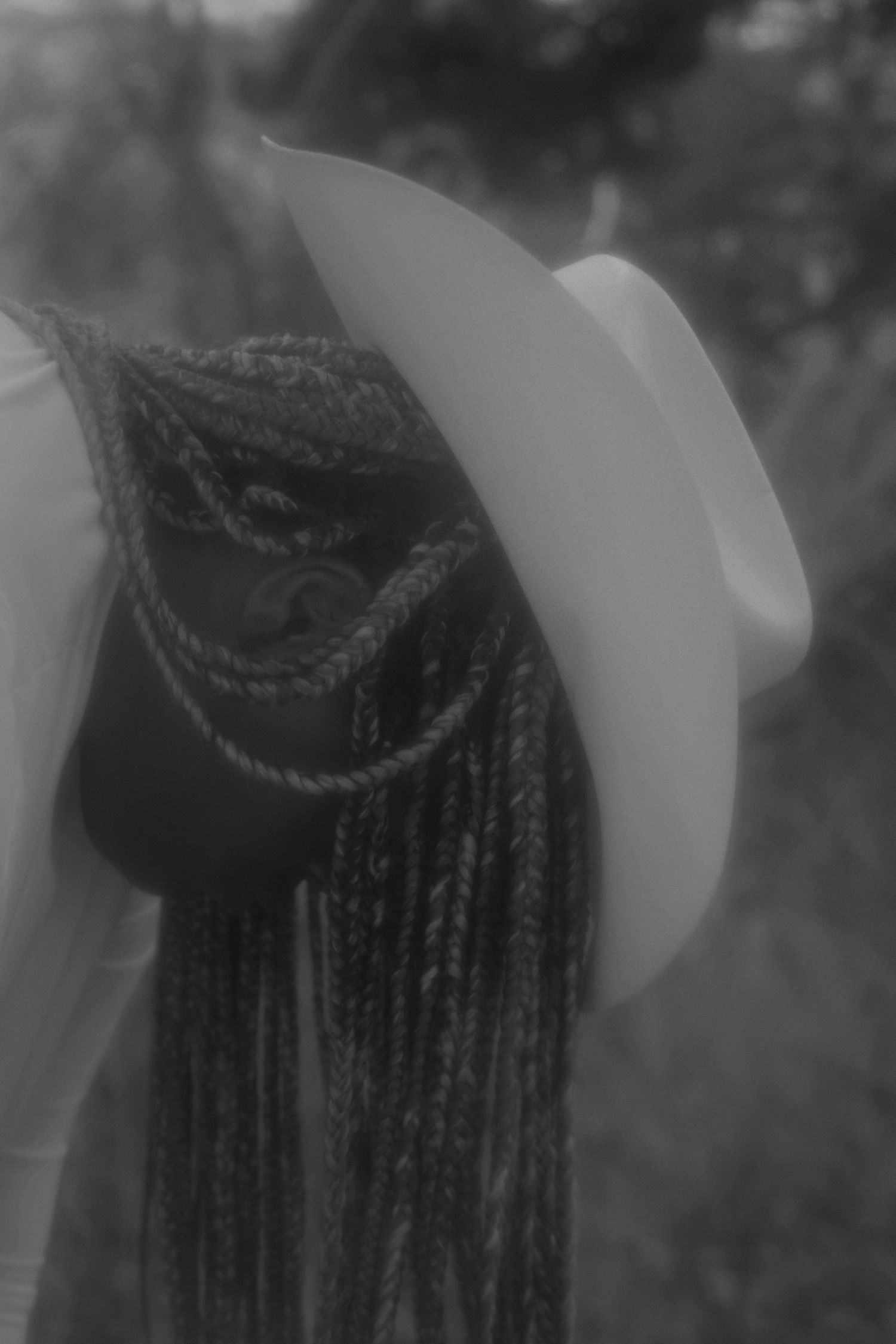 Black and white portrait of woman with braids wearing a white cowboy hat.