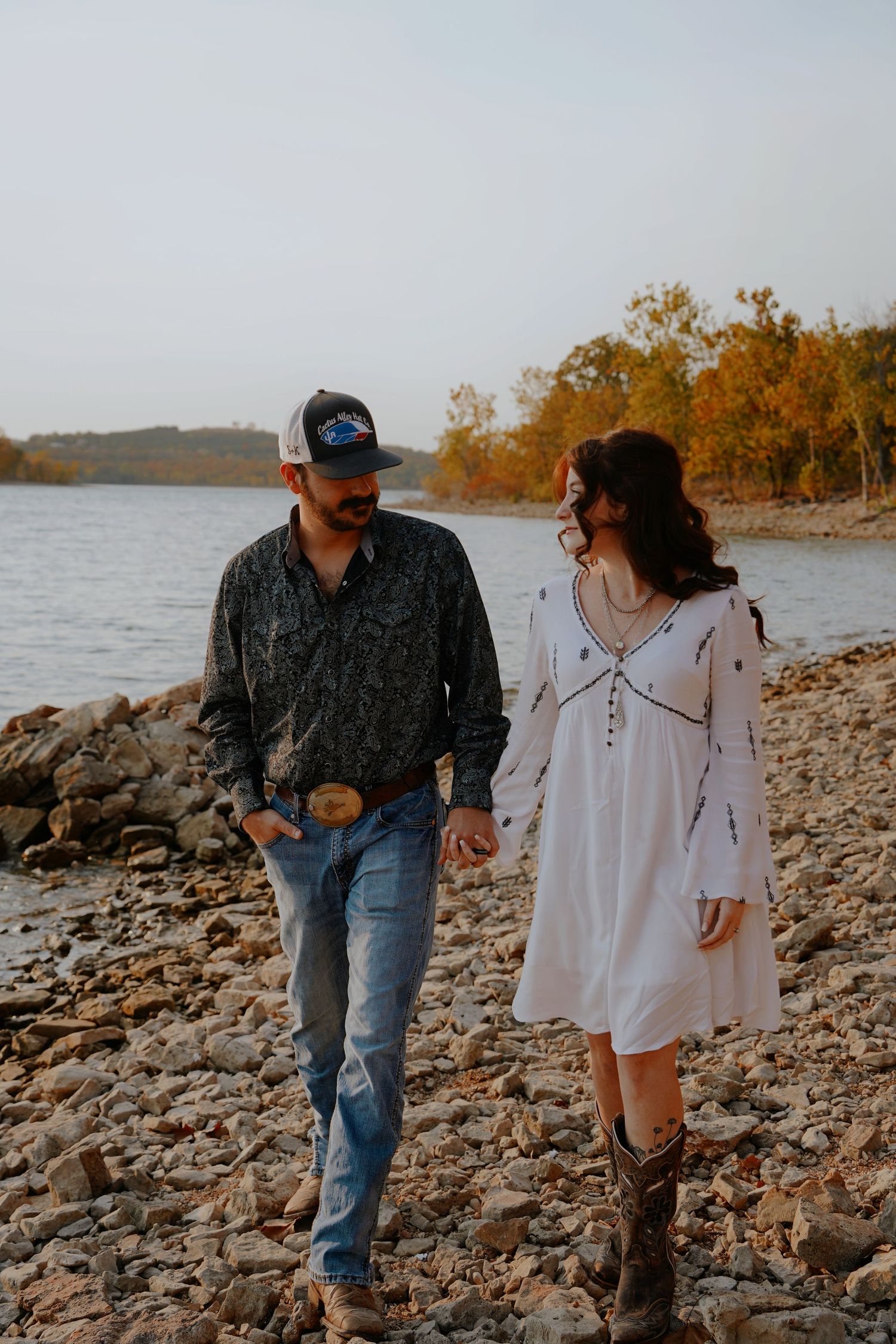 Couple walking hand in hand on rocky lakeshore in autumn setting.