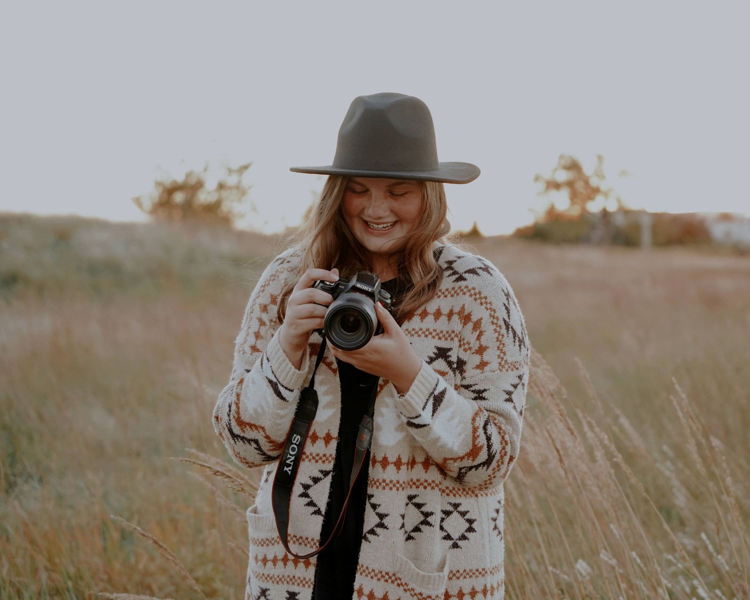 Young woman smiling while looking at camera wearing wide-brim hat in golden field.