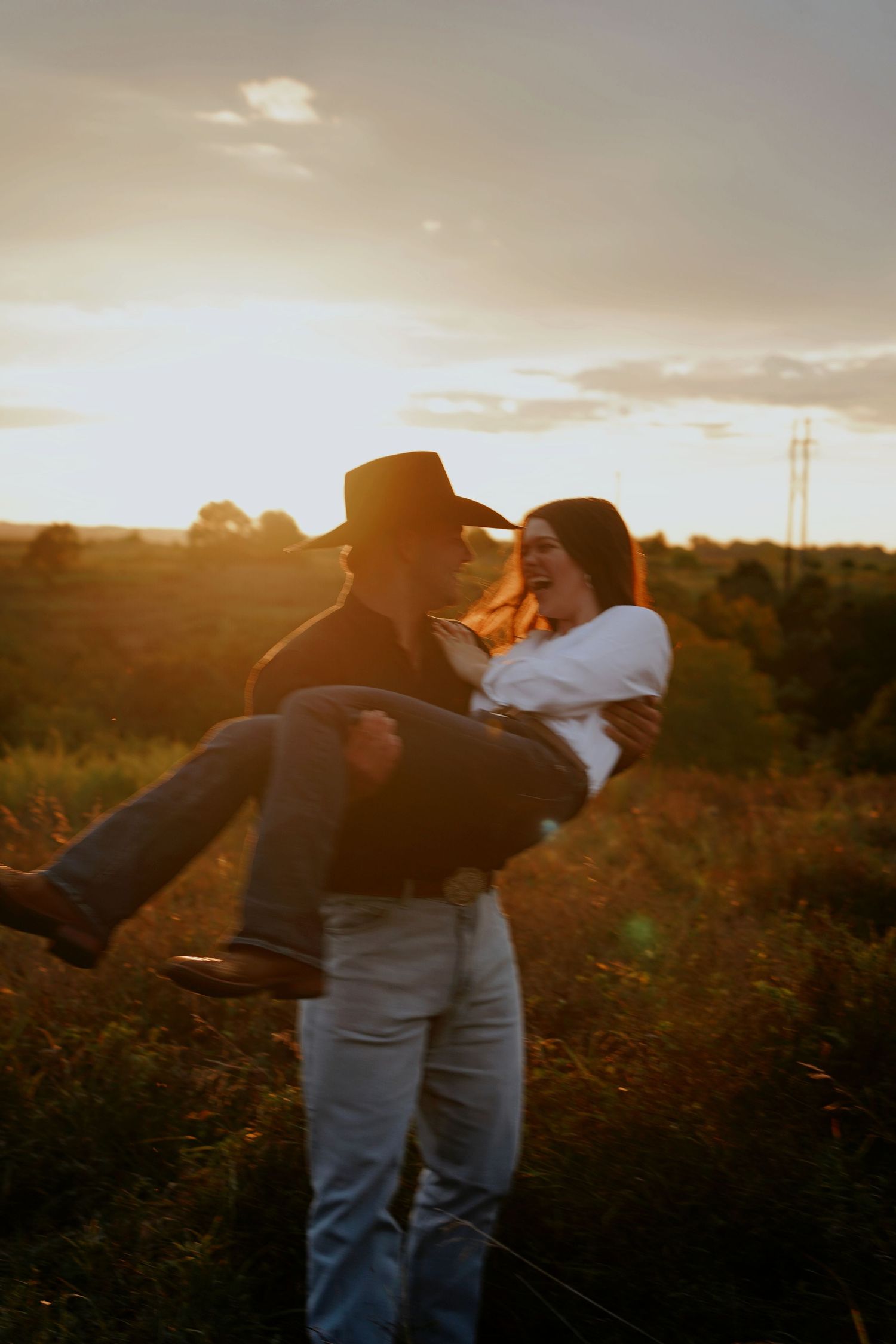 Man in cowboy hat carrying woman at golden sunset in a field.