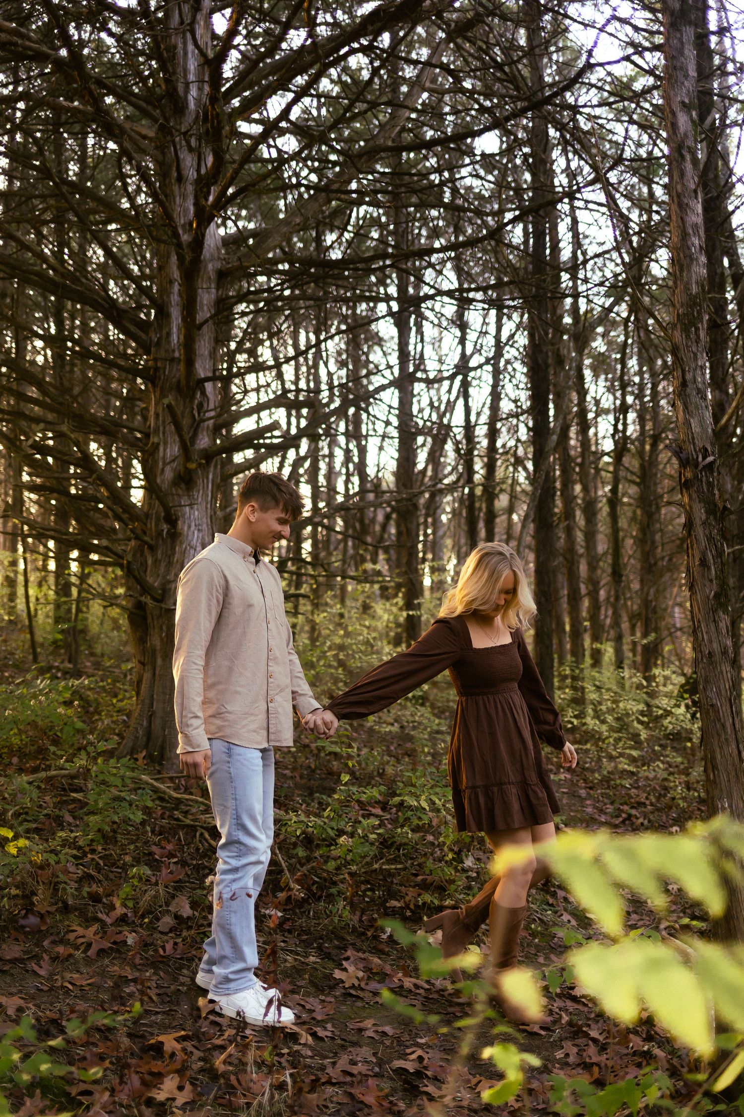 A couple walks through a wooded forest area during an autumn engagement photo session.