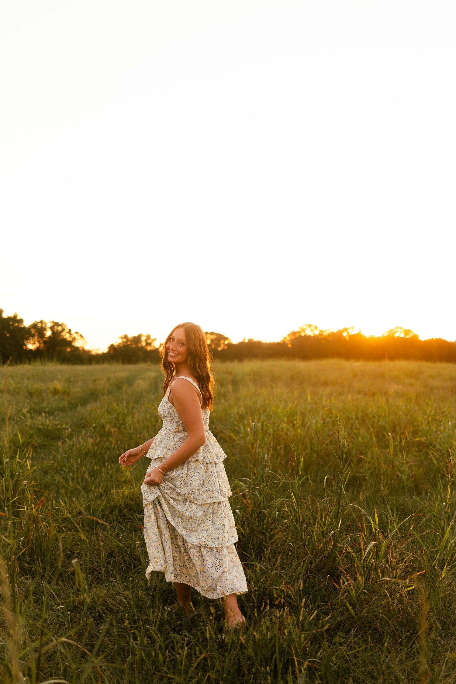 A person in a floral dress twirls joyfully in a sunlit meadow during golden hour.