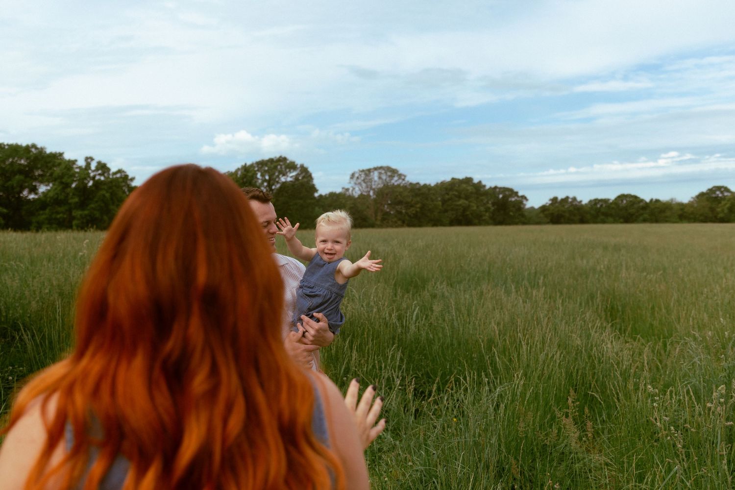 A joyful moment shared between two figures in a sunlit meadow with tall grass and trees in the background.