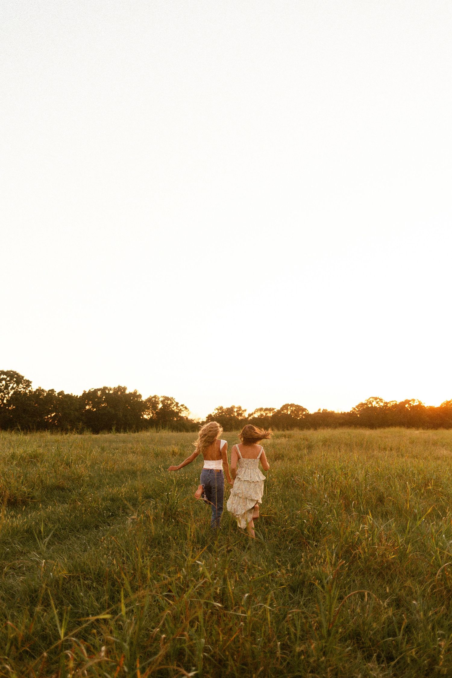 Two people walk through a golden field at sunset while holding hands and enjoying the warm summer evening.