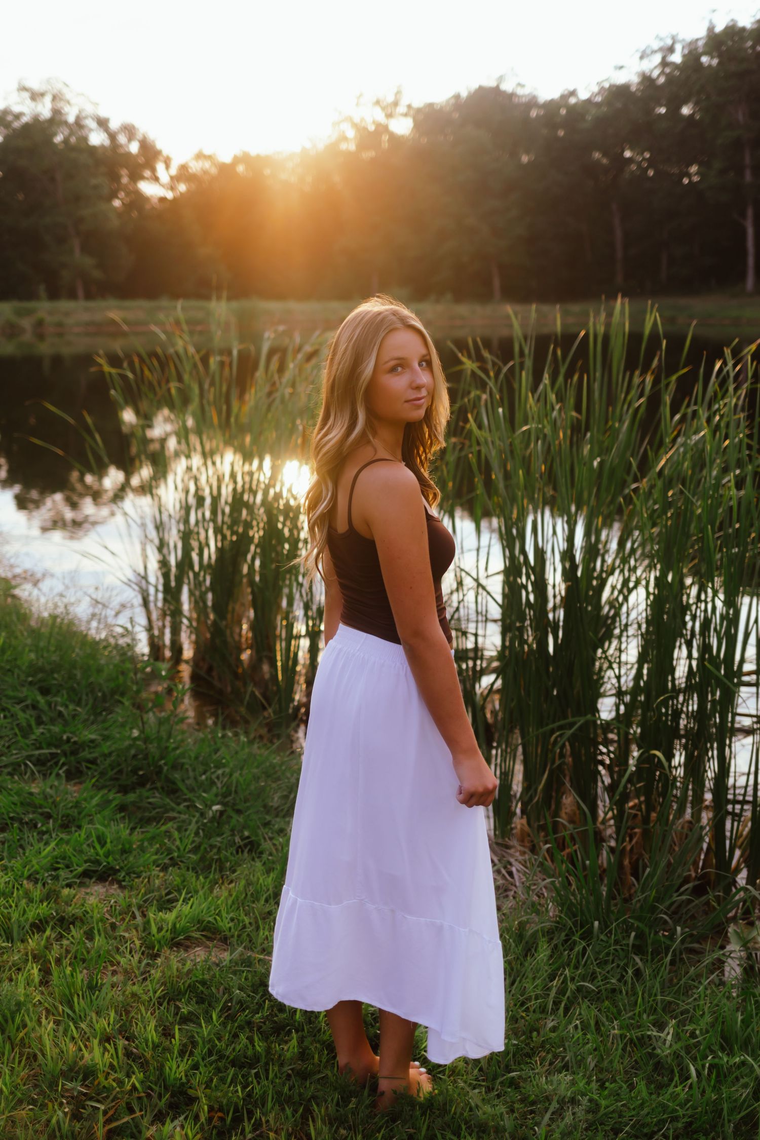A sunset portrait at a pond with tall cattails and golden light creating a dreamy summer evening atmosphere.