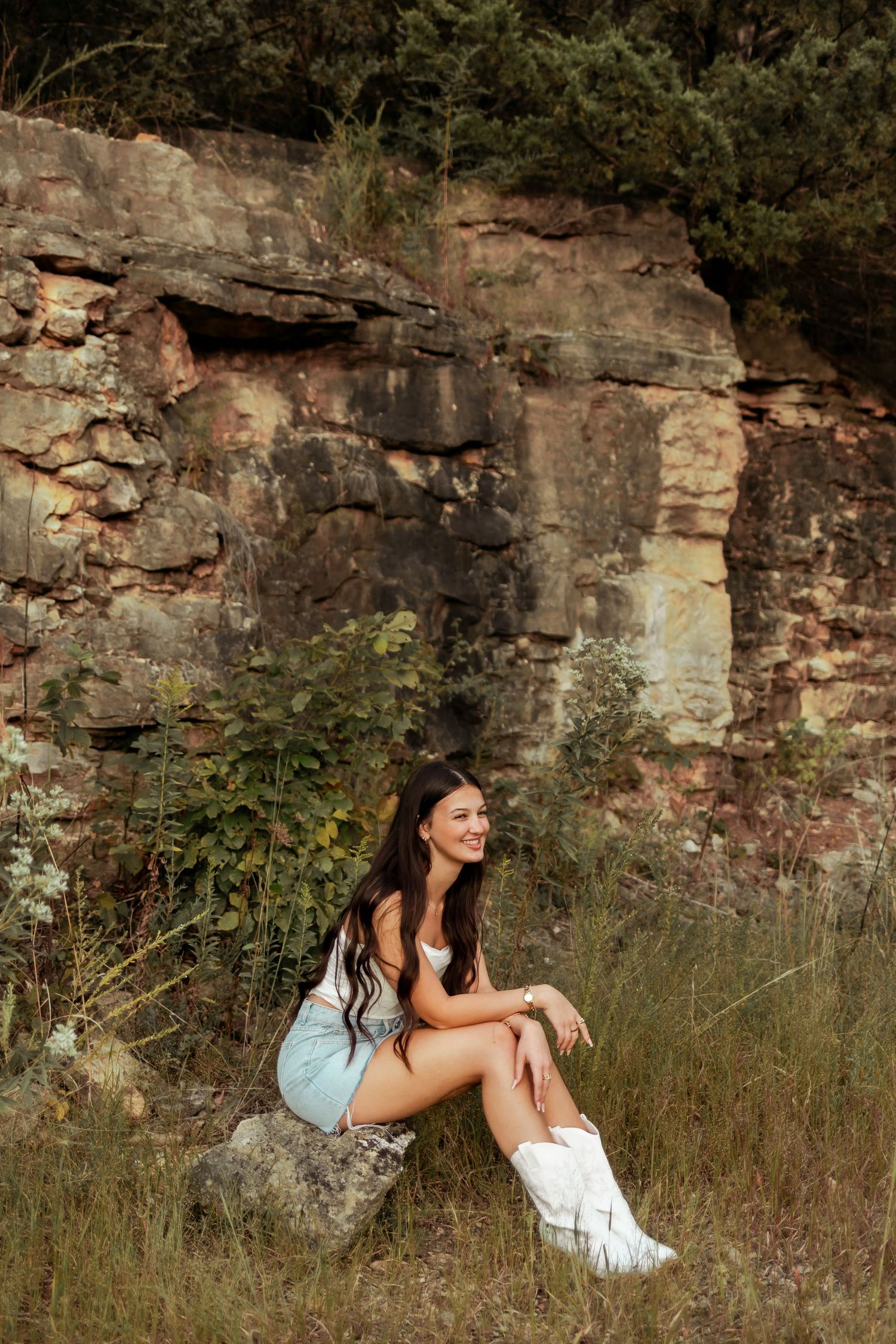A person sits on a rock formation wearing white boots against a rustic stone wall background.