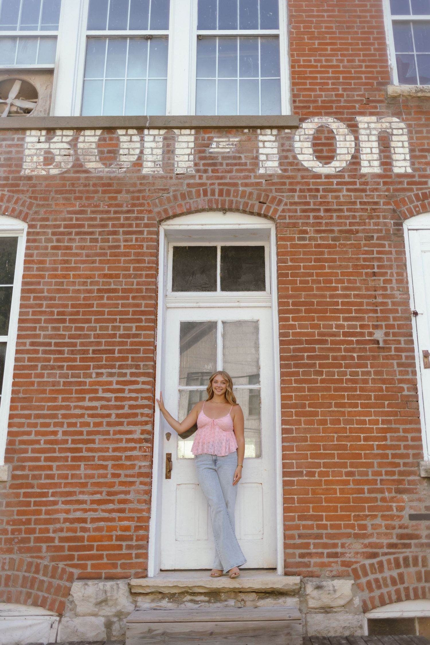 People playfully pose in windows of a historic red brick building with white window frames and trim.