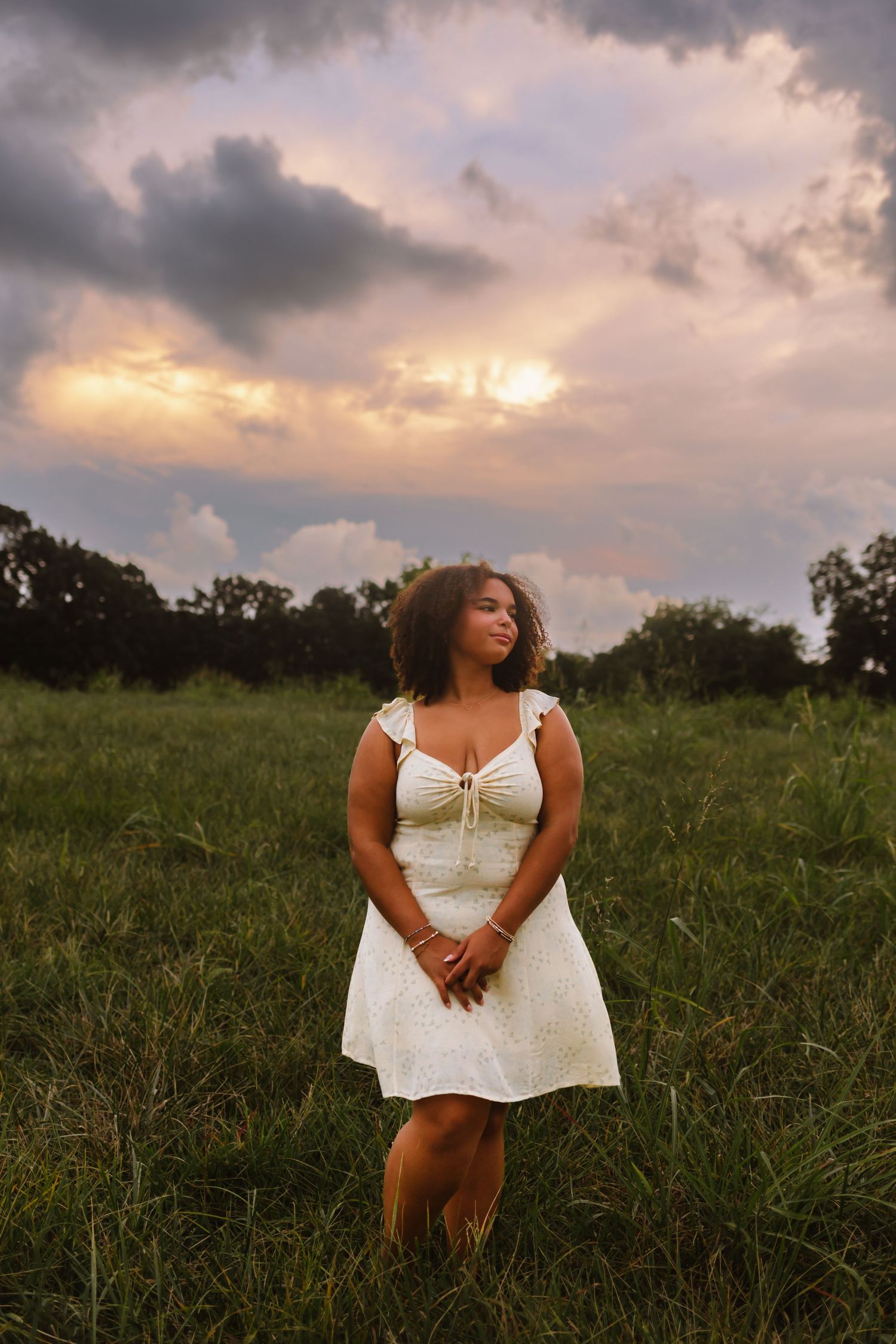 Moody sunset photo series in a grassy meadow featuring a figure in a white dress against dramatic cloudy skies.