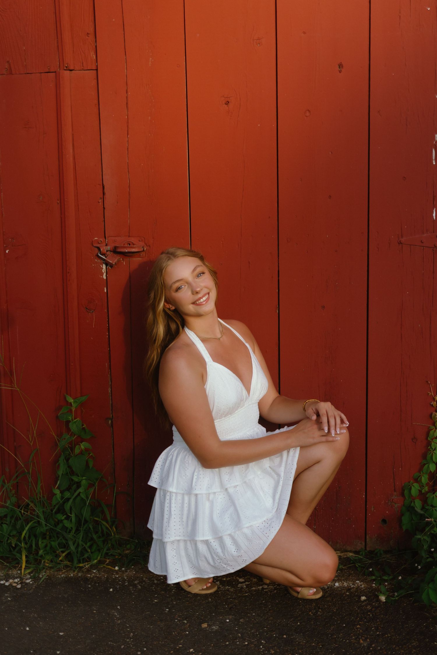 A person in a white sundress poses against a red barn wall in a series of casual outdoor portraits.